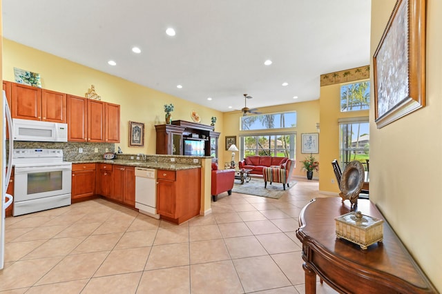 kitchen with white appliances, ceiling fan, light tile patterned floors, light stone counters, and kitchen peninsula