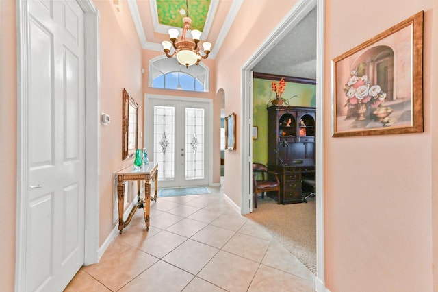 tiled foyer entrance with french doors, a tray ceiling, an inviting chandelier, and crown molding