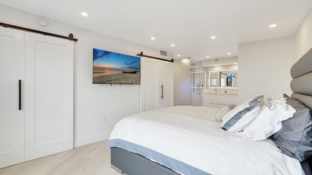 bedroom featuring a barn door, ensuite bathroom, and light hardwood / wood-style floors