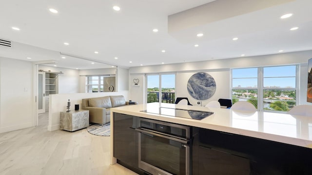 kitchen with black electric stovetop, light wood-type flooring, and stainless steel oven