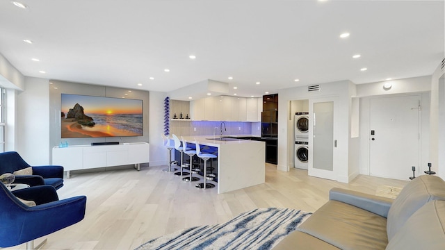 living room with sink, stacked washer and clothes dryer, and light wood-type flooring