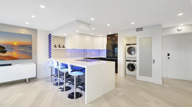 kitchen with kitchen peninsula, tasteful backsplash, a kitchen bar, white cabinetry, and stacked washer / dryer