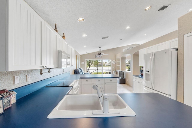 kitchen featuring white cabinetry, white refrigerator with ice dispenser, kitchen peninsula, lofted ceiling, and a textured ceiling