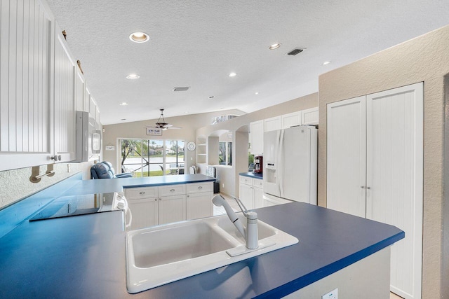 kitchen with a textured ceiling, sink, white cabinets, white fridge with ice dispenser, and lofted ceiling