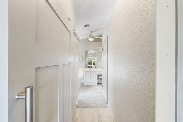 hallway with light wood-type flooring and a textured ceiling