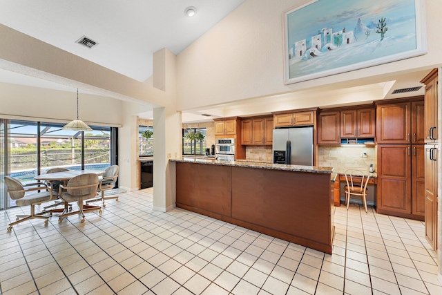 kitchen with light tile patterned floors, appliances with stainless steel finishes, hanging light fixtures, light stone countertops, and kitchen peninsula