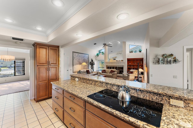 kitchen featuring ceiling fan, light stone counters, black electric stovetop, a fireplace, and ornamental molding