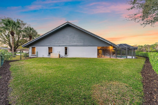 back house at dusk featuring a pool, a lanai, and a lawn