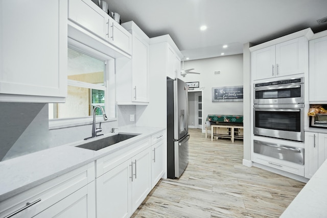 kitchen with light stone countertops, stainless steel appliances, ceiling fan, sink, and white cabinetry