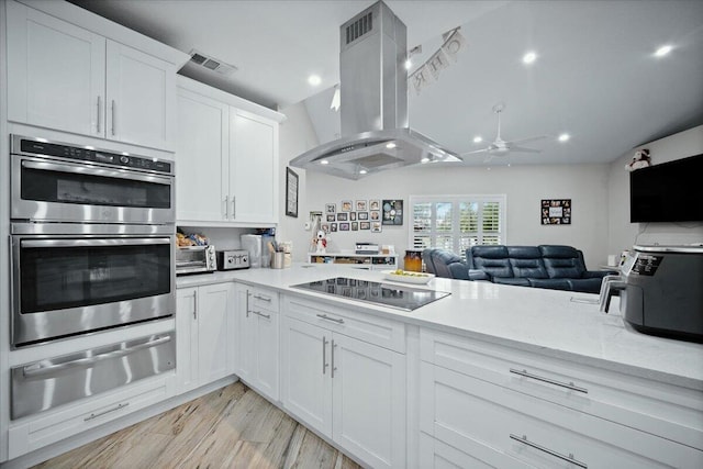 kitchen featuring black electric stovetop, stainless steel double oven, island range hood, light hardwood / wood-style flooring, and white cabinets