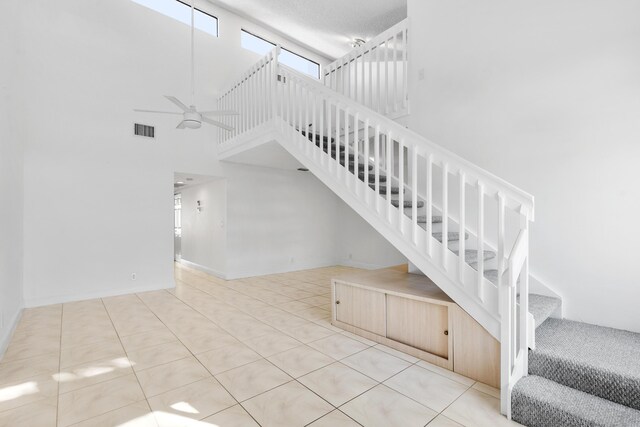 stairs featuring tile patterned flooring, a textured ceiling, a towering ceiling, and ceiling fan