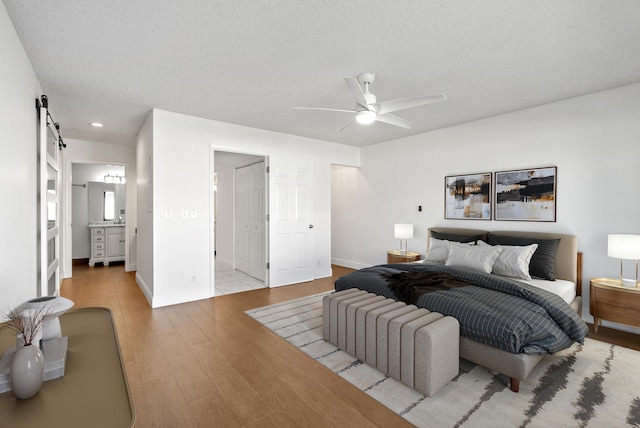 bedroom featuring ensuite bath, ceiling fan, a barn door, a textured ceiling, and light hardwood / wood-style floors