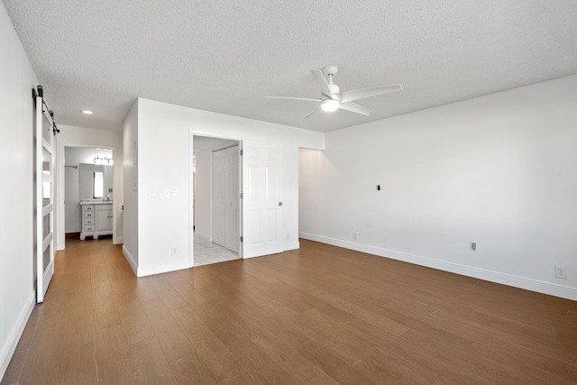 unfurnished bedroom featuring ceiling fan, a barn door, ensuite bathroom, light hardwood / wood-style floors, and a textured ceiling