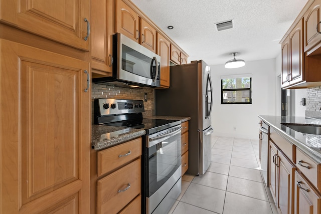 kitchen featuring tasteful backsplash, dark stone counters, a textured ceiling, light tile patterned floors, and appliances with stainless steel finishes