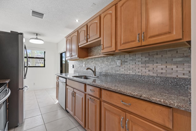 kitchen featuring sink, dark stone countertops, a textured ceiling, light tile patterned flooring, and stainless steel appliances