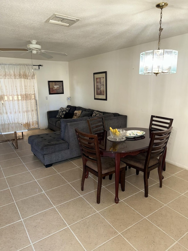 dining space featuring tile patterned flooring, ceiling fan with notable chandelier, and a textured ceiling