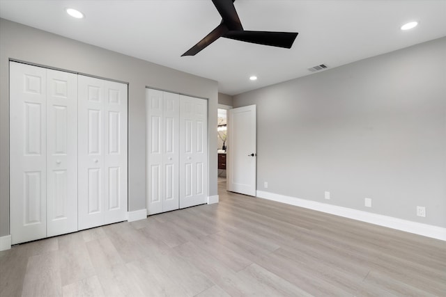 unfurnished bedroom featuring ceiling fan, light wood-type flooring, and two closets