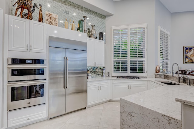 kitchen with sink, light tile patterned flooring, light stone countertops, appliances with stainless steel finishes, and white cabinets