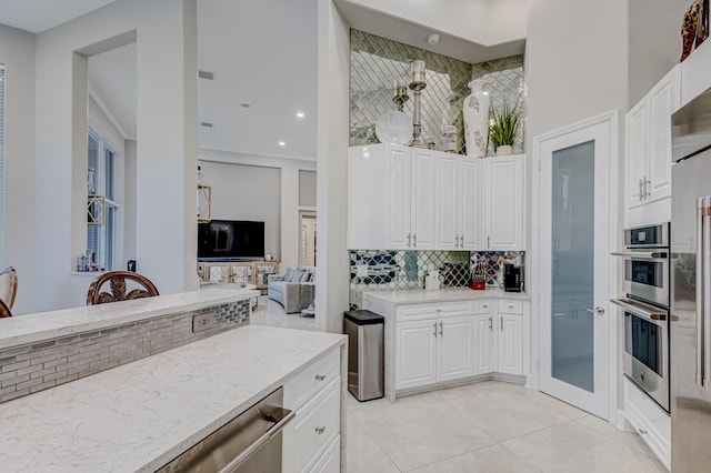 kitchen with light stone countertops, stainless steel double oven, white cabinetry, tasteful backsplash, and light tile patterned flooring