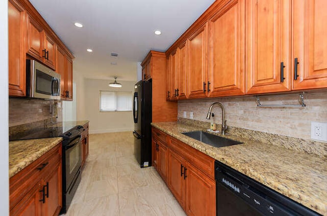 kitchen with backsplash, light stone countertops, sink, and black appliances