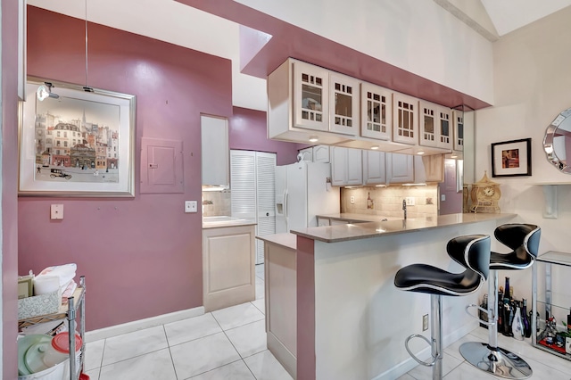 kitchen featuring white fridge with ice dispenser, a kitchen breakfast bar, backsplash, kitchen peninsula, and light tile patterned floors