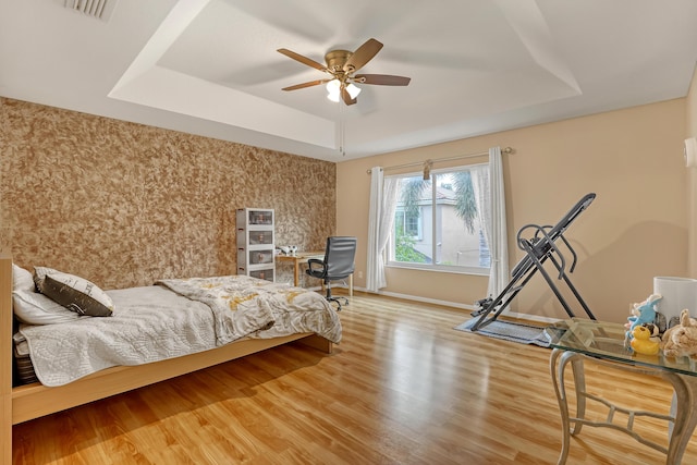 bedroom featuring ceiling fan, a raised ceiling, and wood-type flooring