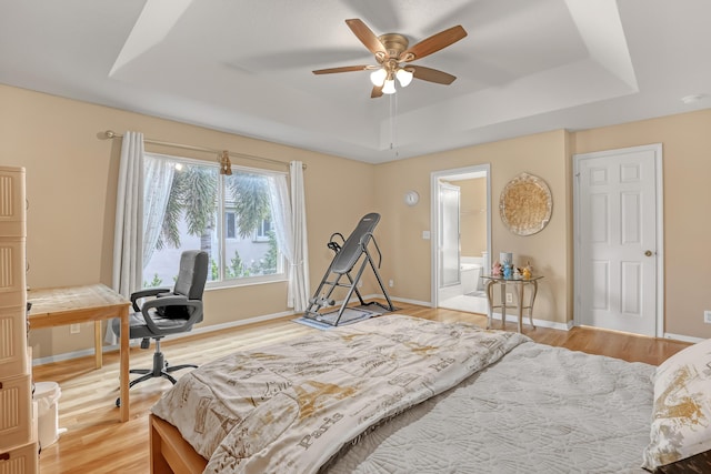 bedroom featuring ceiling fan, ensuite bath, hardwood / wood-style flooring, and a tray ceiling