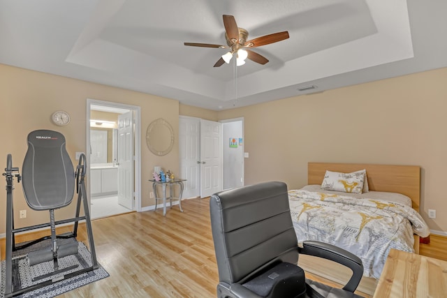 bedroom featuring ensuite bath, a raised ceiling, ceiling fan, and light hardwood / wood-style flooring