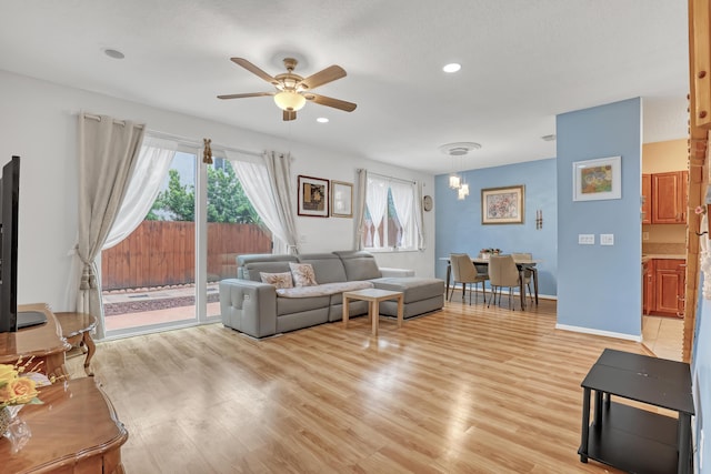 living room featuring ceiling fan with notable chandelier and light hardwood / wood-style floors