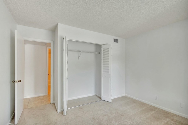 unfurnished bedroom featuring a textured ceiling, light colored carpet, and a closet