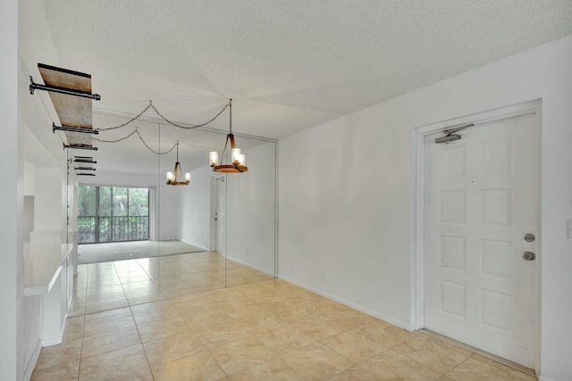 tiled empty room featuring a textured ceiling and a chandelier