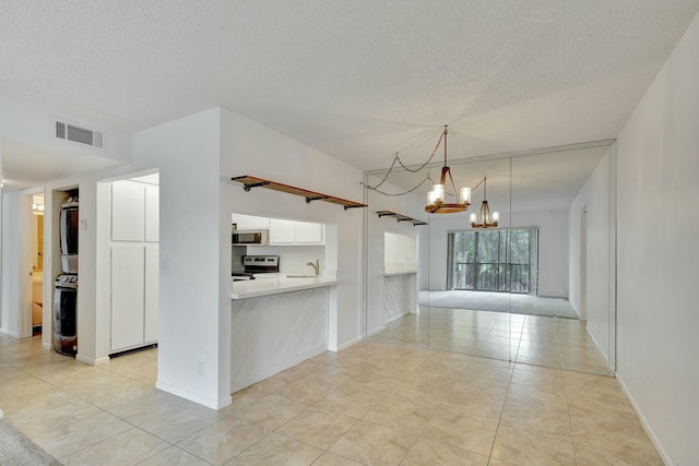 kitchen featuring pendant lighting, white cabinets, a chandelier, stacked washer / drying machine, and stainless steel range with electric cooktop