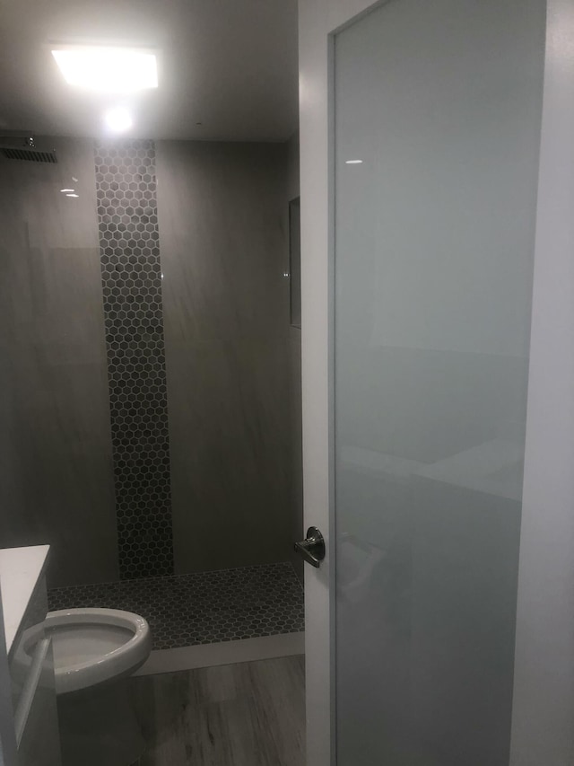 bathroom featuring tiled shower, vanity, toilet, and hardwood / wood-style floors