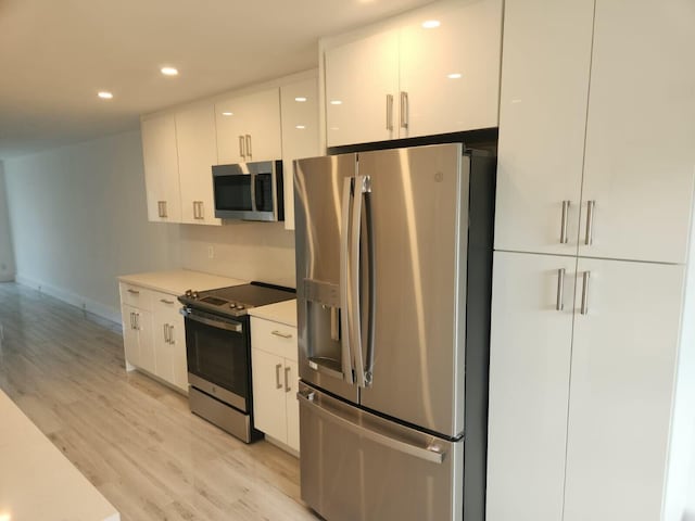 kitchen with appliances with stainless steel finishes, white cabinets, and light hardwood / wood-style floors