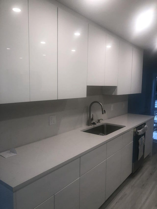 kitchen featuring white cabinetry, sink, dishwashing machine, decorative backsplash, and light wood-type flooring