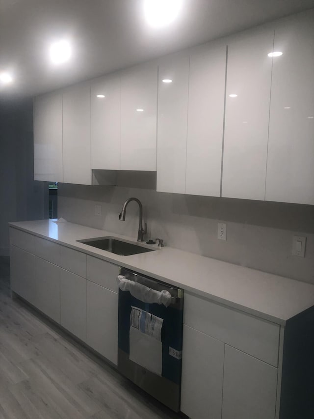 kitchen with sink, dishwasher, tasteful backsplash, light hardwood / wood-style floors, and white cabinets