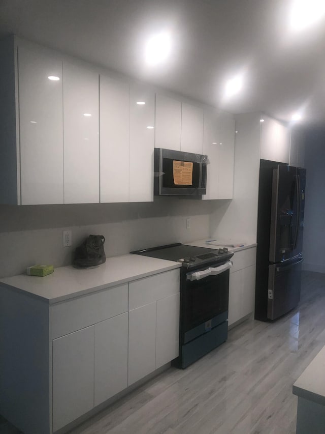 kitchen with light hardwood / wood-style flooring, white cabinets, and black appliances