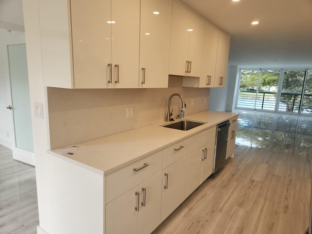 kitchen with sink, white cabinetry, tasteful backsplash, stainless steel dishwasher, and light hardwood / wood-style floors