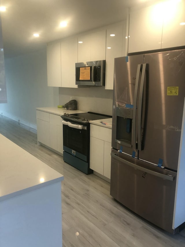 kitchen with stainless steel appliances, white cabinets, and light wood-type flooring