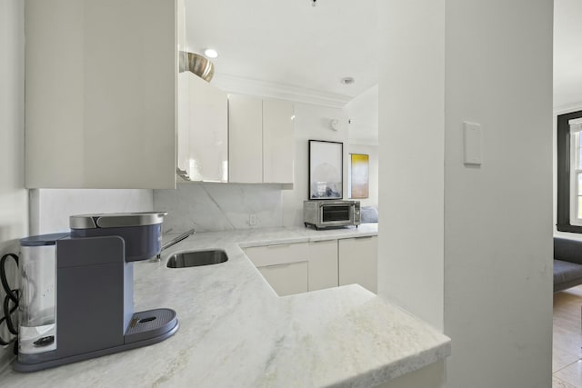 kitchen featuring white cabinets, crown molding, sink, light stone countertops, and tasteful backsplash