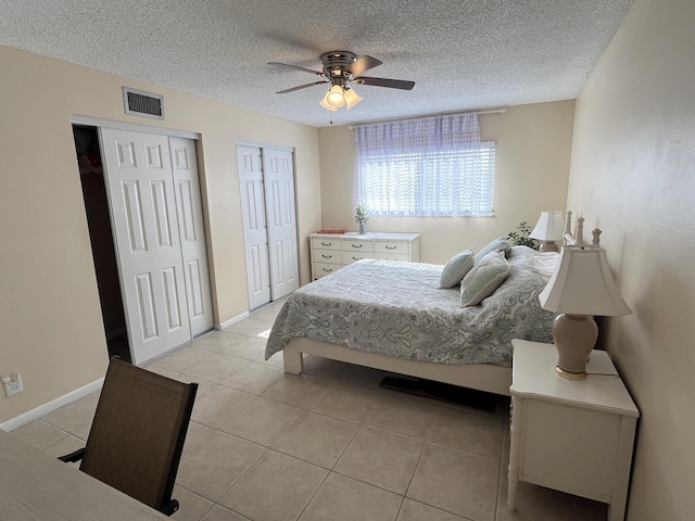 bedroom with ceiling fan, light tile patterned flooring, a textured ceiling, and multiple closets