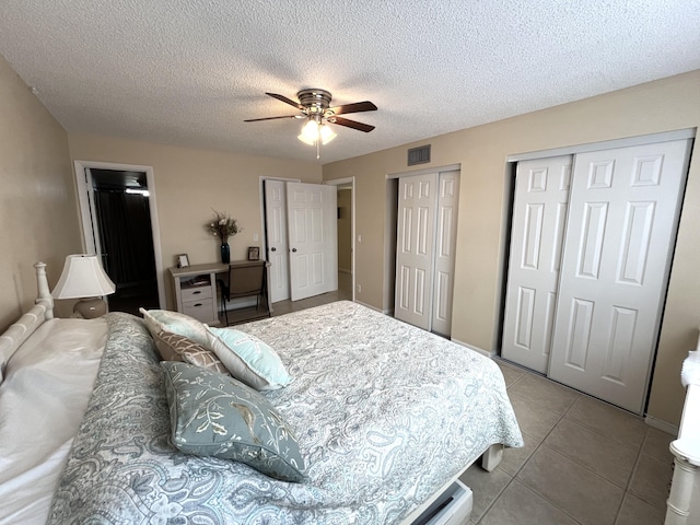 tiled bedroom with ceiling fan, a textured ceiling, and multiple closets