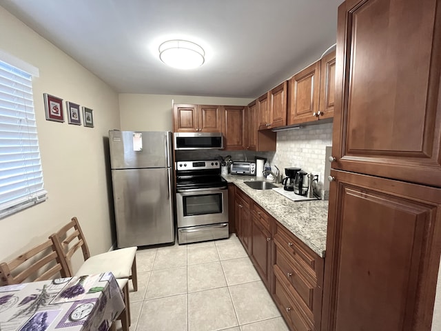 kitchen featuring sink, light stone countertops, appliances with stainless steel finishes, tasteful backsplash, and light tile patterned flooring