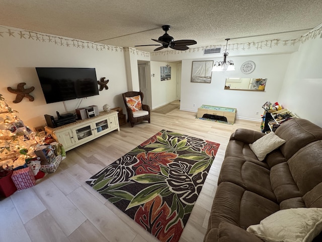 living room featuring ceiling fan with notable chandelier, light hardwood / wood-style floors, and a textured ceiling