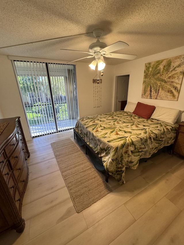 bedroom with access to exterior, ceiling fan, expansive windows, and a textured ceiling