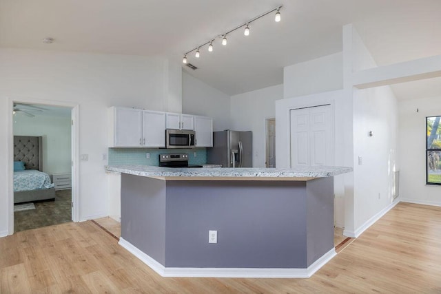 kitchen with white cabinetry, light stone countertops, stainless steel appliances, tasteful backsplash, and light wood-type flooring