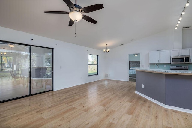 unfurnished living room with rail lighting, ceiling fan with notable chandelier, light hardwood / wood-style flooring, and vaulted ceiling