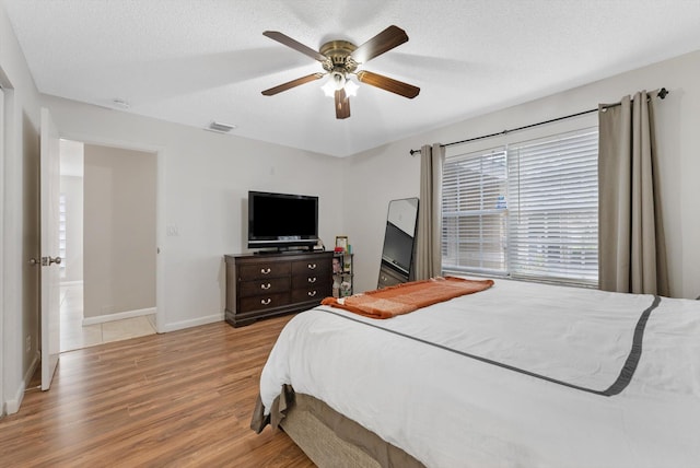 bedroom with ceiling fan, light hardwood / wood-style floors, and a textured ceiling