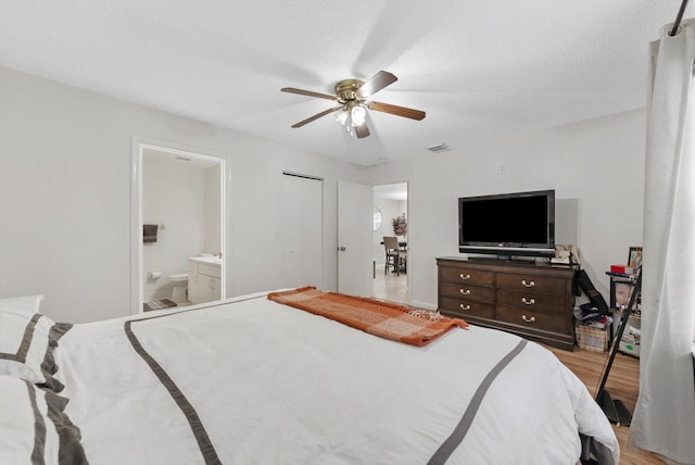 bedroom featuring ceiling fan, light wood-type flooring, a textured ceiling, and ensuite bath