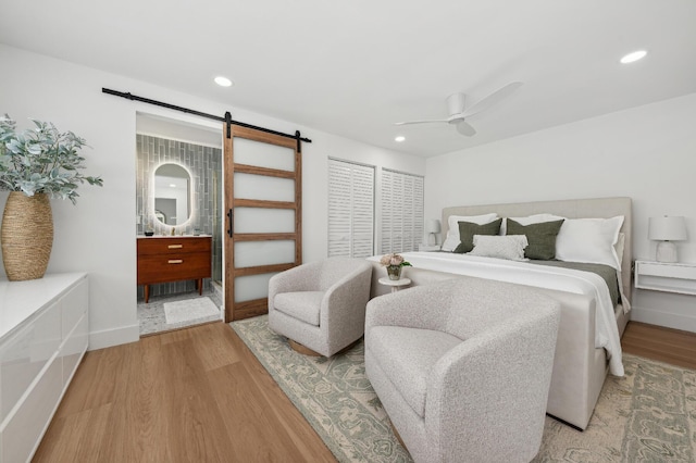 bedroom featuring light wood-type flooring, a barn door, and ceiling fan